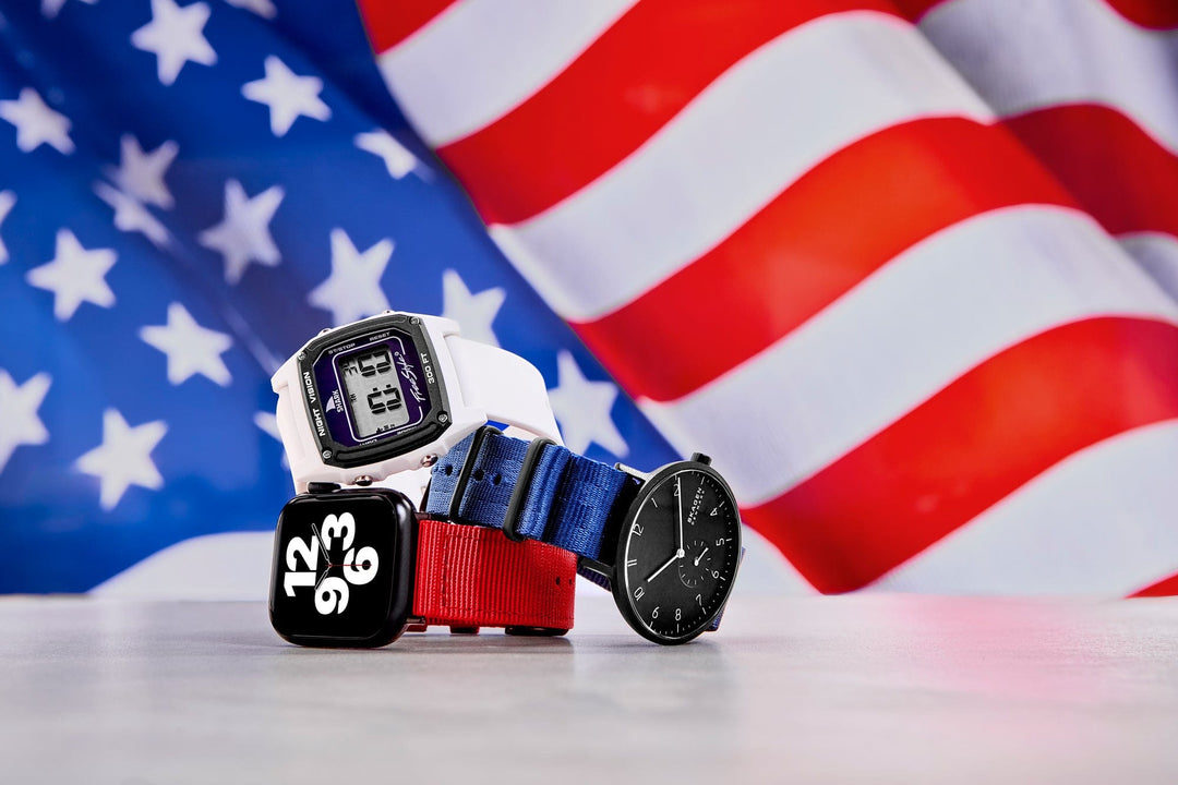Three watches with red, white, and blue straps displayed in front of an American flag backdrop