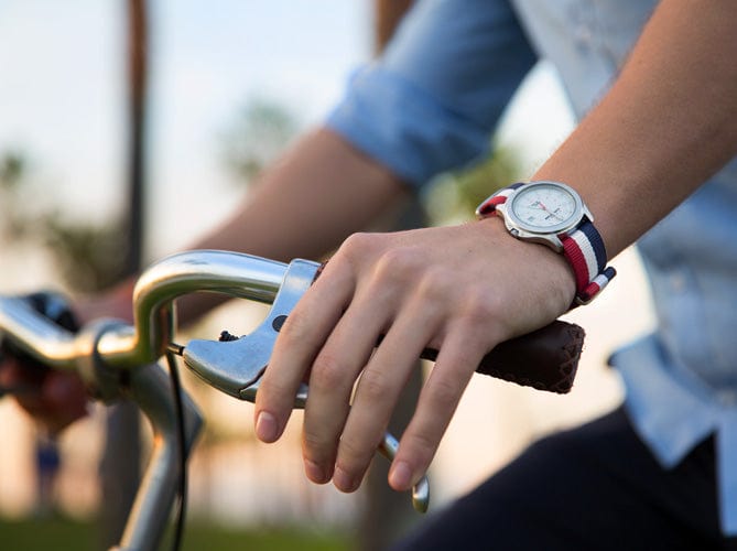 Person wearing a watch with a red, white, and navy striped military style strap on a bicycle