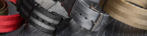 Close-up row of seat belt military style watch straps in black, gray, khaki, red, and charcoal