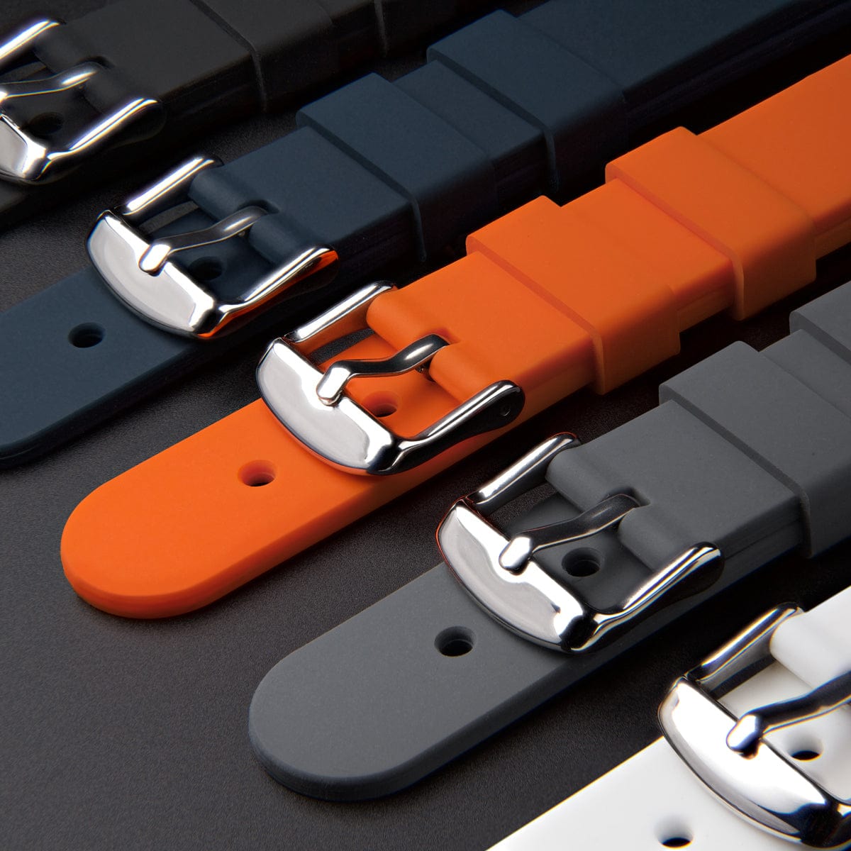 Multiple silicone watch straps in black, orange, and gray lined up showing buckles